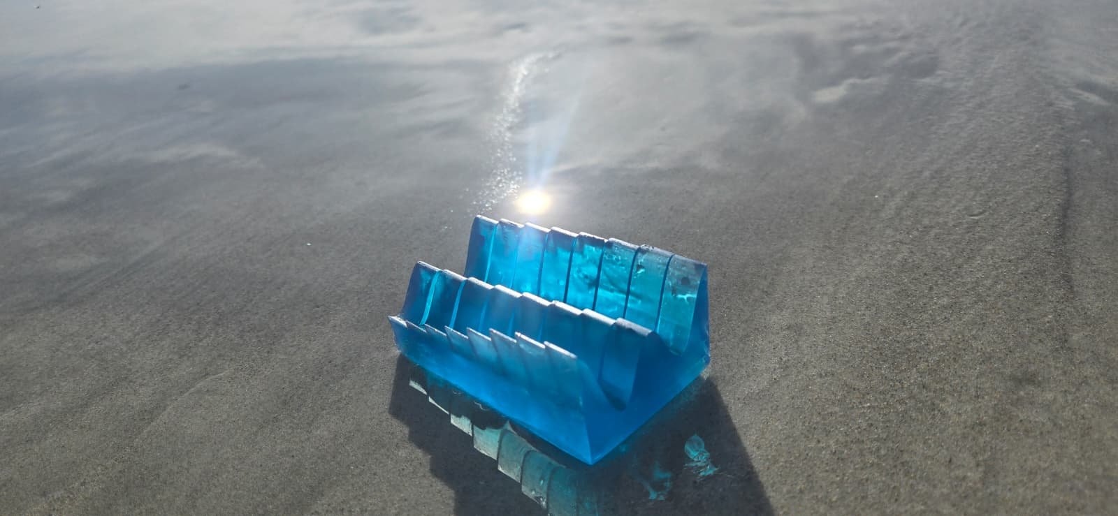 Translucent blue resin tide keepsake glowing on wet beach sand at the Florida coast